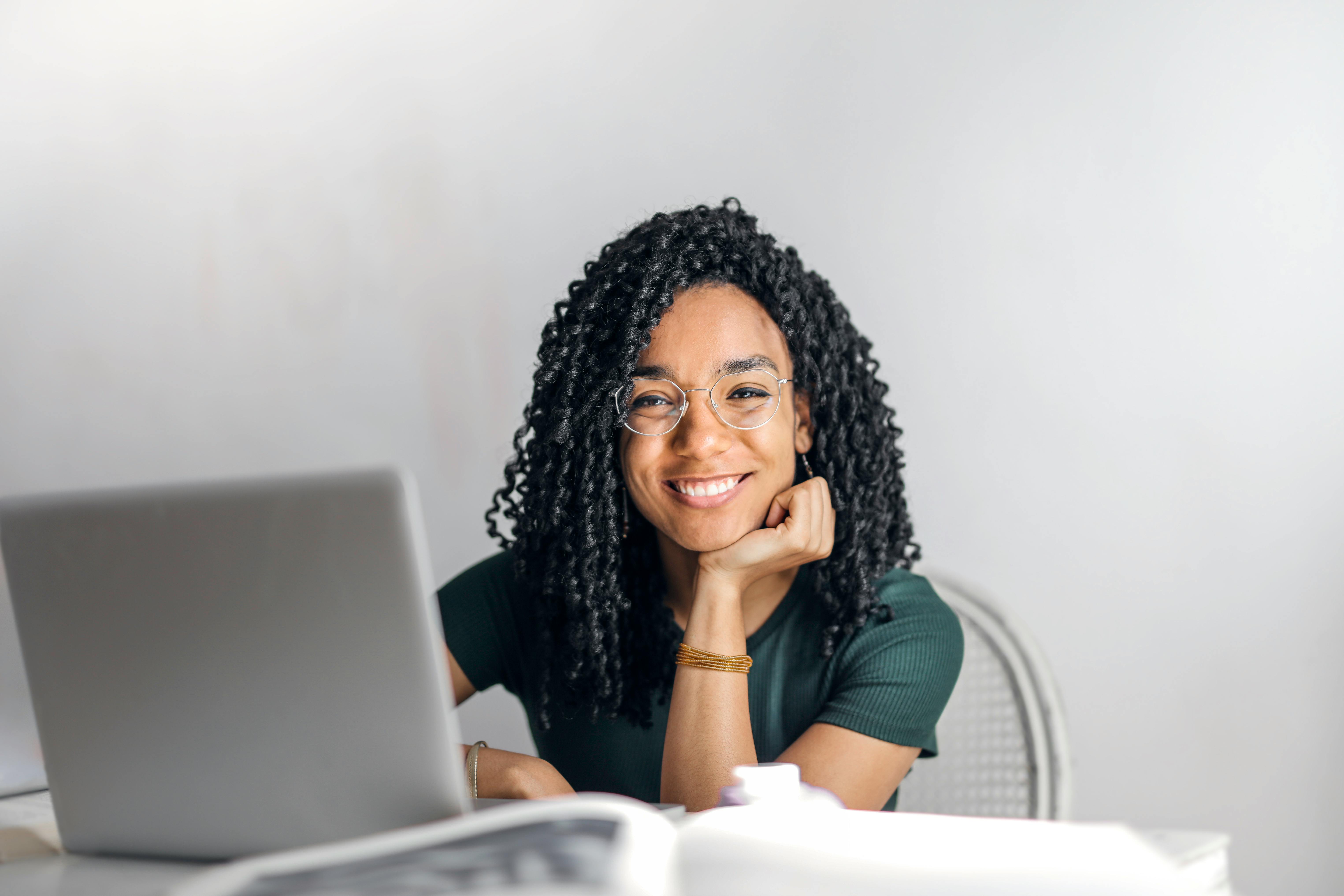 A woman sitting behind a laptop computer, smiling at the camera
